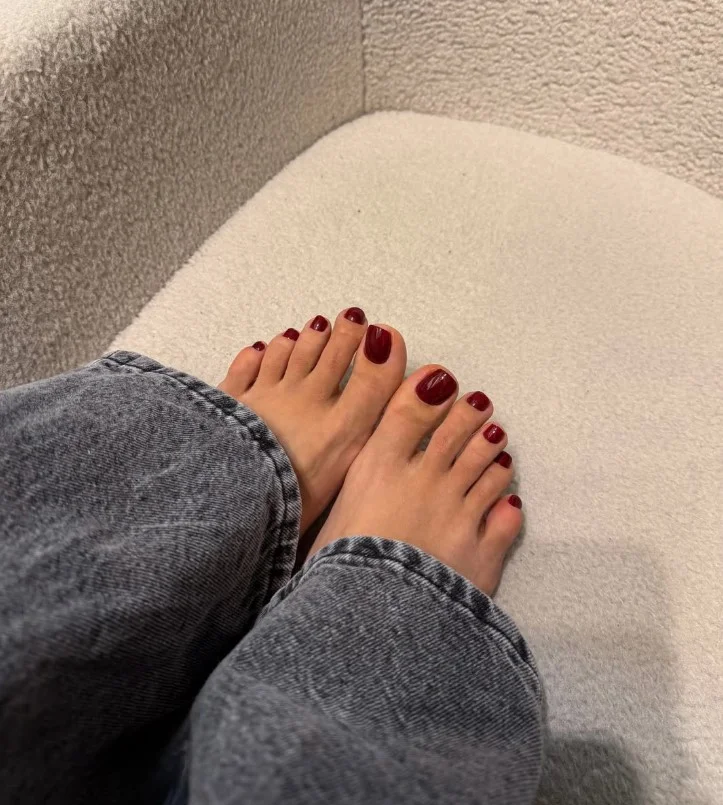 Glossy burgundy fall toe nail designs on neatly shaped toenails with cozy autumn styling.