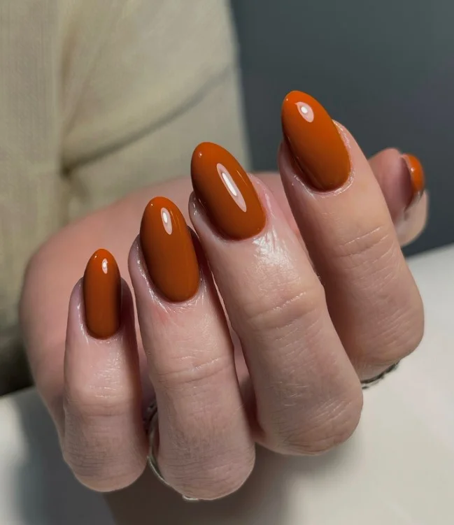 Burnt orange manicure on tan skin with glossy short nails.