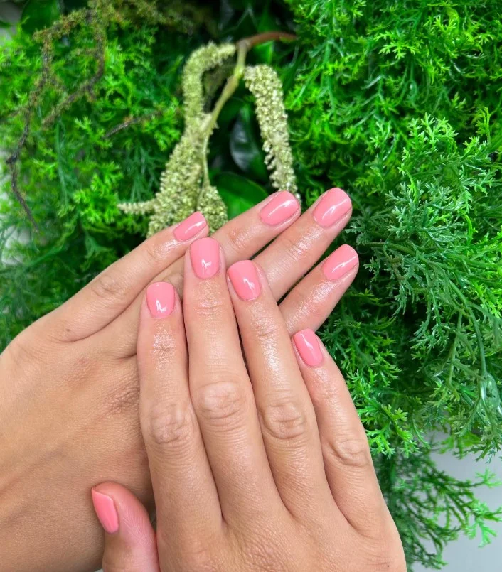 Coral pink nail polish on tan skin for a bright summer manicure.