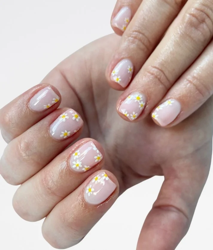 Cute daisy flower nail designs on a sheer nude base with glossy almond-shaped nails.
