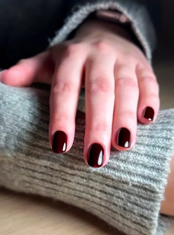 Deep burgundy nails on pale skin with an elegant glossy finish