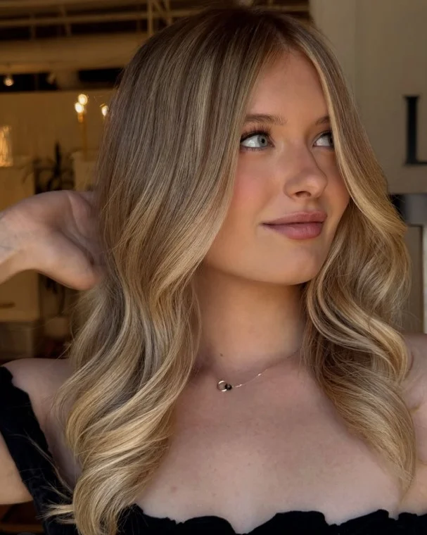 Honey blonde hair color on warm olive skin with soft layered waves and glossy shine.