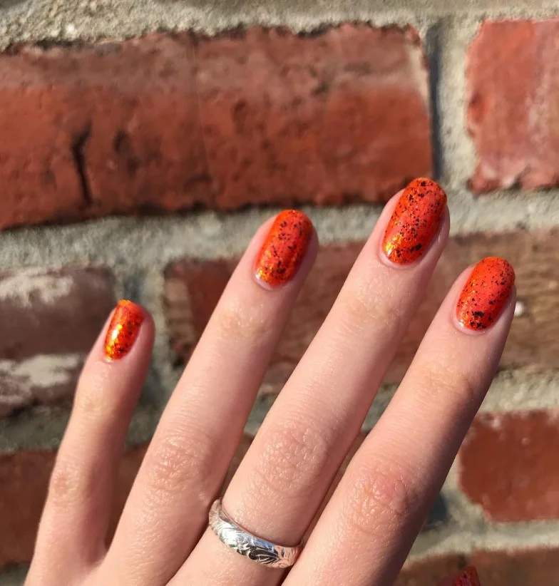 Jack-o'-lantern Halloween nail art with smiling pumpkin faces on orange nails.
