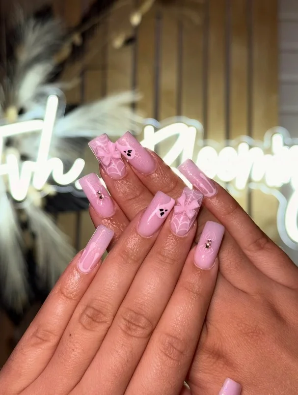 Pink coquette Halloween nails with black bows and tiny spooky nail art.