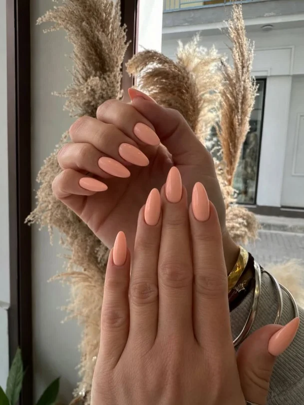 Soft peach nail polish on tan skin with a fresh glossy finish.