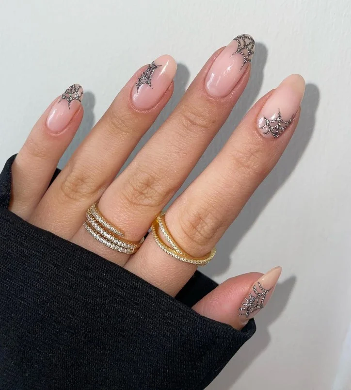 Nude Halloween nails featuring delicate black spider web nail art on short almond nails.