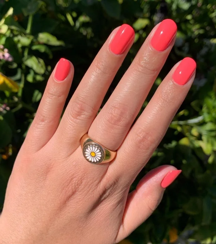 Warm coral nail polish on pale skin for a bright summer manicure