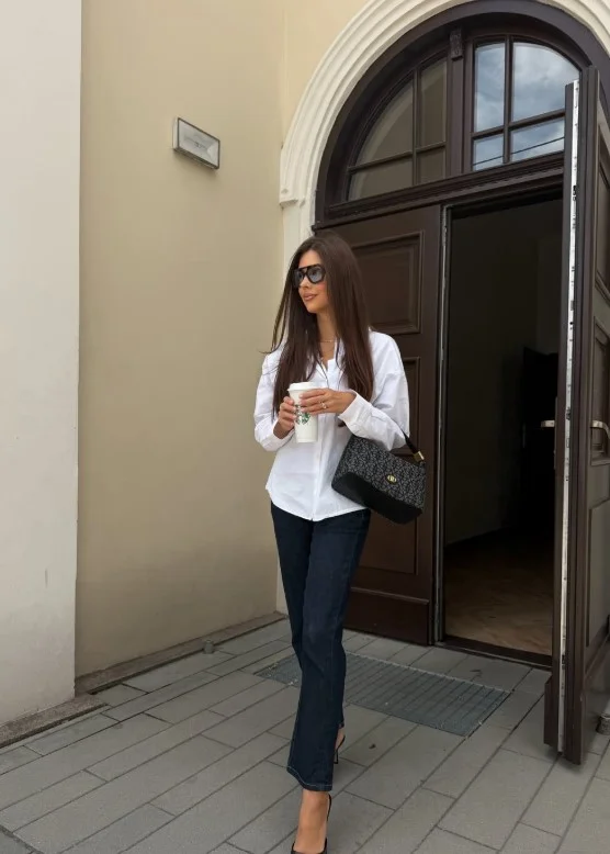 Woman styling high waisted jeans with a crisp white button-down shirt and loafers