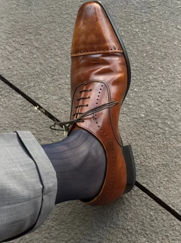 Cognac leather shoes styled with light grey dress pants and a blue blazer.