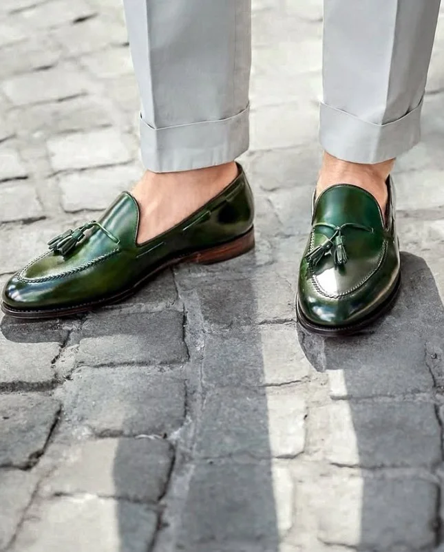 Dark green leather loafers paired with grey trousers in a polished men's smart-casual outfit.
