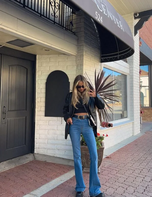 Woman styling high waisted flare jeans with a fitted top and heeled boots
