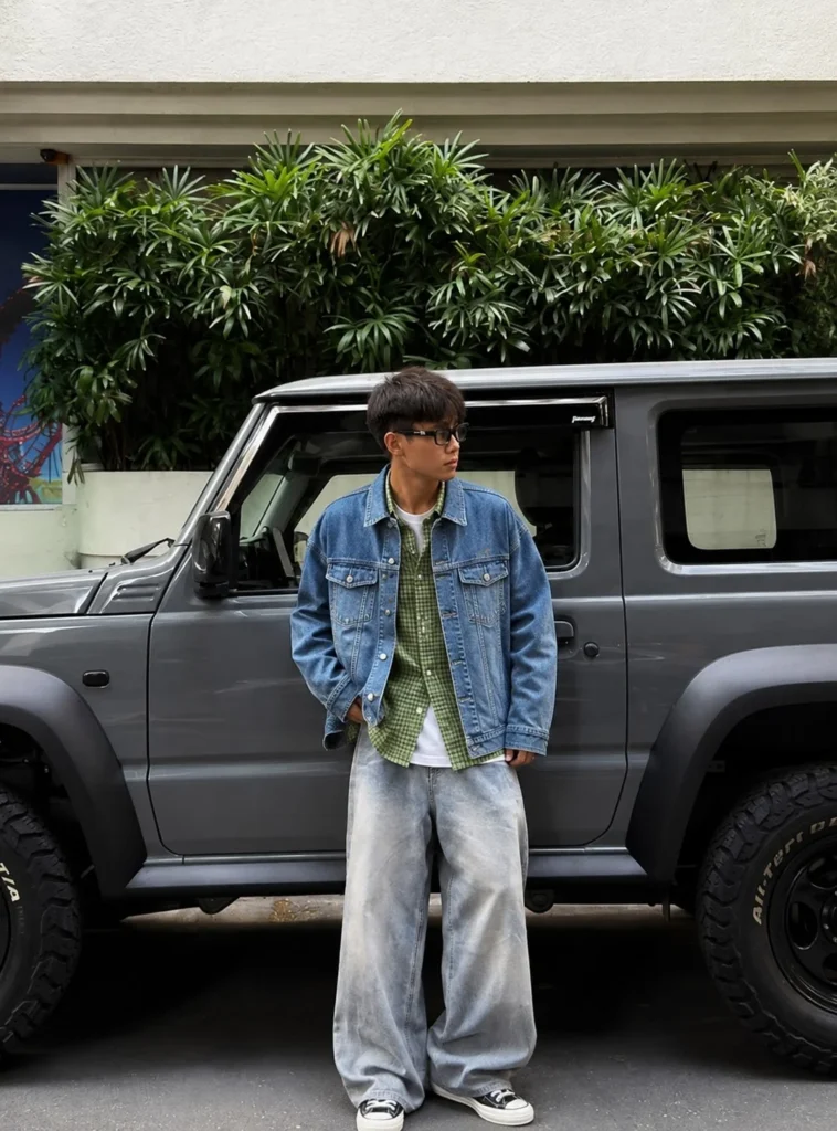 Green flannel layered under a denim jacket with dark jeans