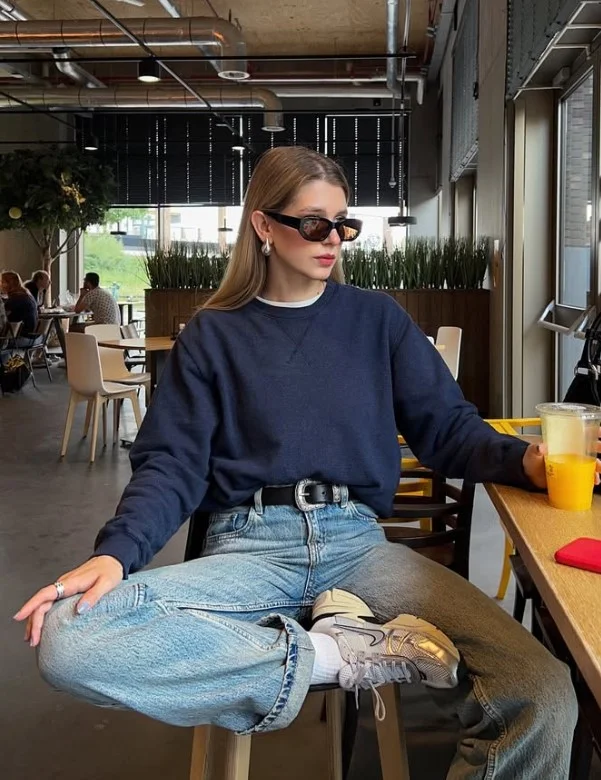 Woman styling light-wash jeans with a navy knit top and classic loafers