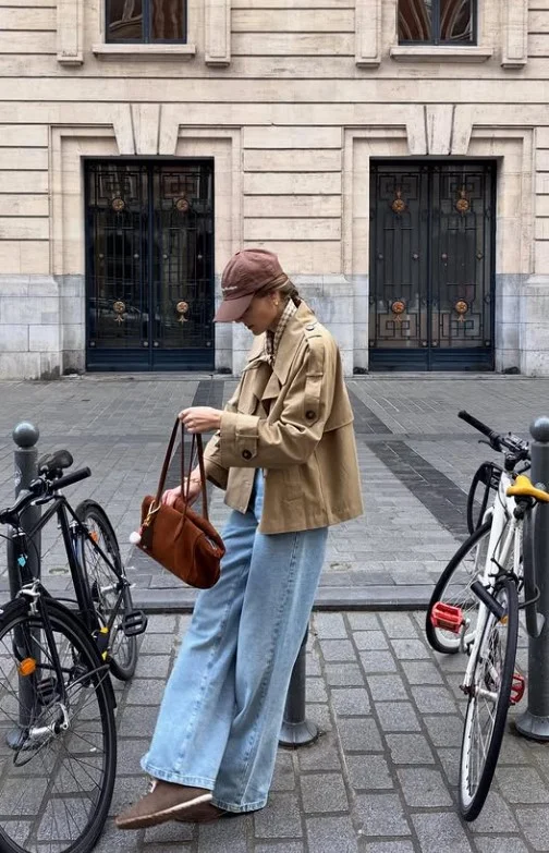 Woman styling light jeans with a beige trench coat and polished flats