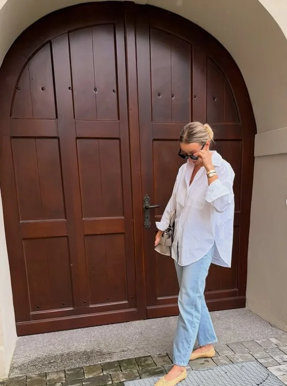 Woman wearing light straight-leg jeans with a relaxed white button-down shirt and brown leather accessories