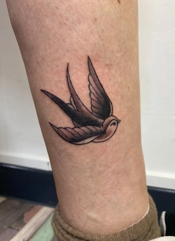 American traditional swallow tattoo on a woman's lower leg