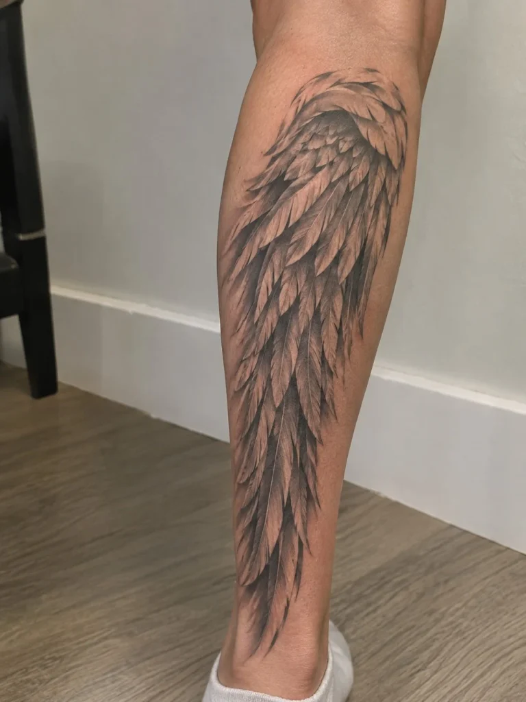 Angel wing lower leg tattoo with detailed feathers and graceful lines