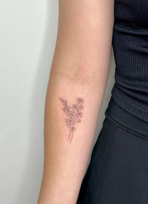 Birth flower forearm tattoo featuring a delicate botanical stem and detailed bloom