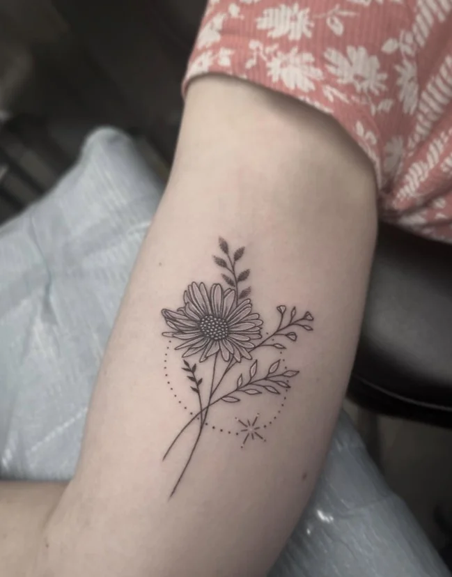 Birth flower tattoo with a delicate stem placed on the inner upper arm