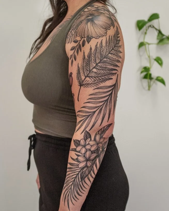 Blackwork fern and botanical arm wrap tattoo with bold dark leaves