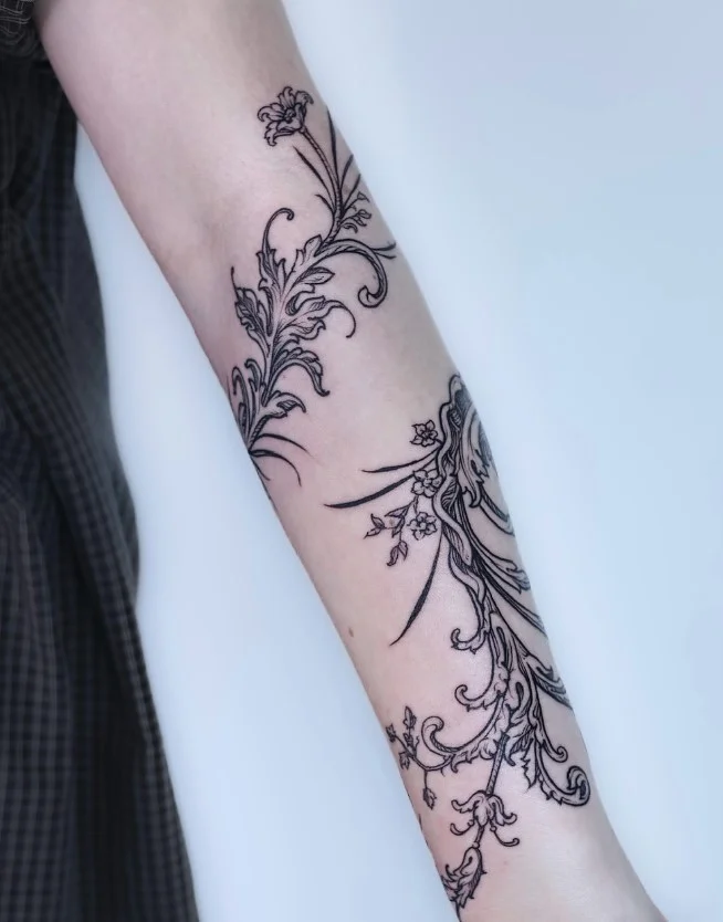 Bold blackwork flowers and leafy branches wrapping around a woman's forearm tattoo