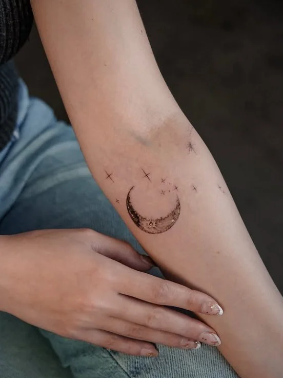 Crescent moon and stars tattoo arranged vertically on the inner forearm