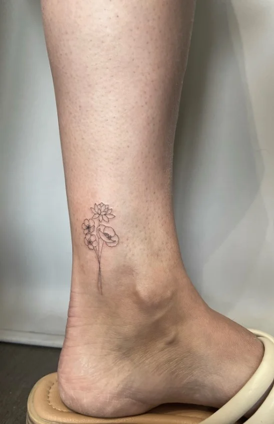 Fine line birth flower ankle tattoo featuring a delicate botanical flower with a slender stem and detailed floral outline