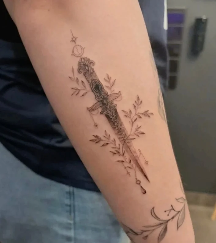 Upper forearm tattoo women fine-line dagger botanical tattoo