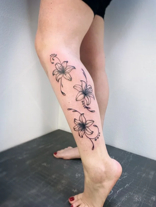 Fine-line floral lower leg tattoo with a delicate flower and slender stem
