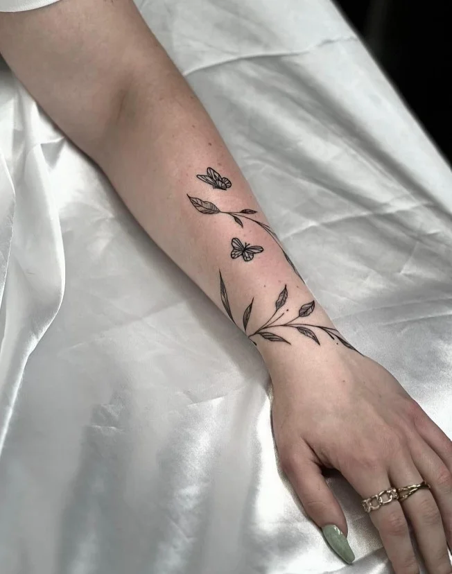 Fine-line floral wrap around arm tattoo with delicate flowers and leaves