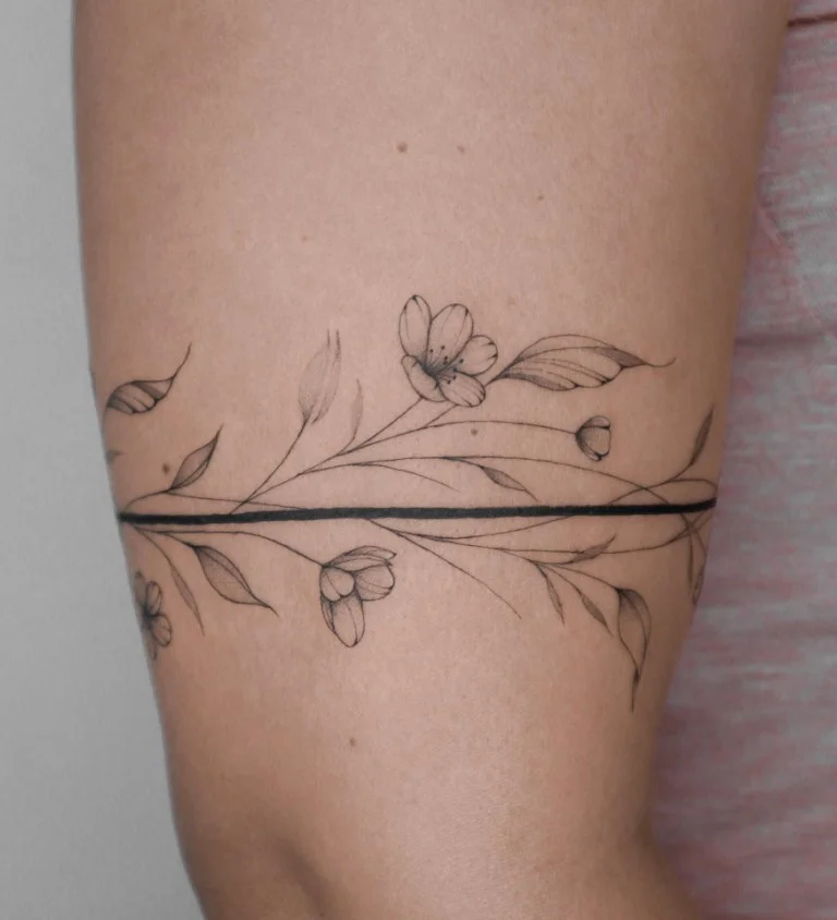 Fine-line floral wrap around bicep tattoo with delicate flowers and leaves