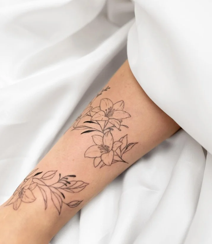 Delicate fine-line flowers and thin leafy stems wrapping around a woman's forearm