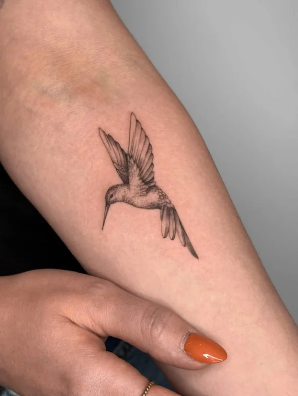 Fine-line hummingbird tattoo with delicate details on the inner forearm