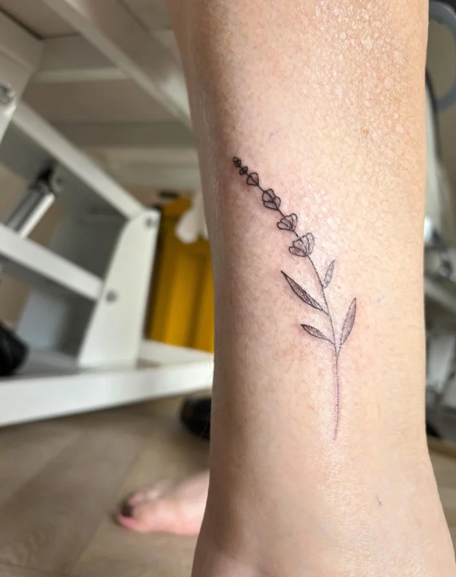 Fine line lavender ankle tattoo featuring a delicate lavender sprig with thin stems and small flowers along the ankle