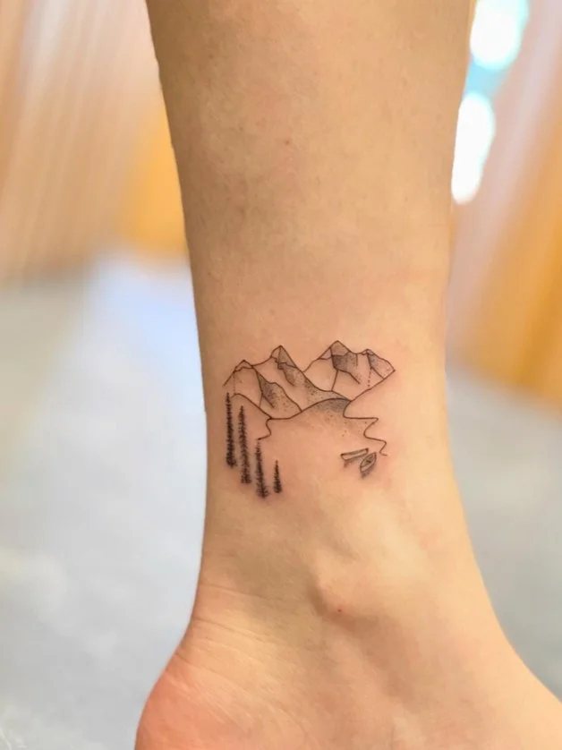 Fine line mountain ankle tattoo featuring a minimalist mountain range outline placed delicately above the ankle bone