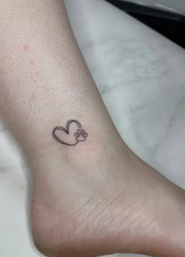 Fine line paw print ankle tattoo featuring a small minimalist paw print design placed delicately above the ankle bone