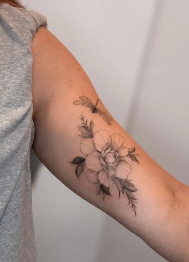 Fine-line peony tattoo on the inner upper arm with a long curved stem