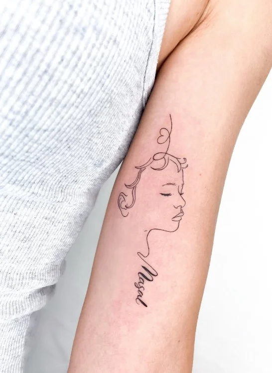 Fine-line feminine portrait tattoo on the inner upper arm