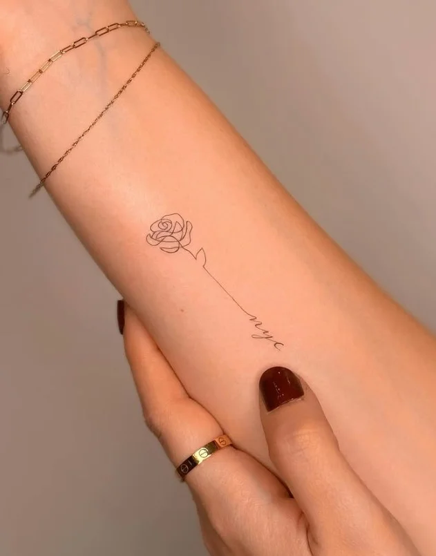 Fine-line rose tattoo with a long stem placed vertically on the inner forearm