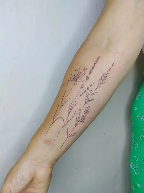 Fine-line wildflower stem tattoo running vertically along the inner forearm