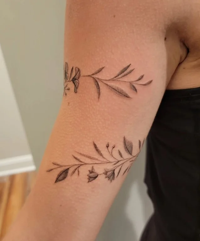 Flowing vine and leaf bicep wrap tattoo following the curve of the upper arm