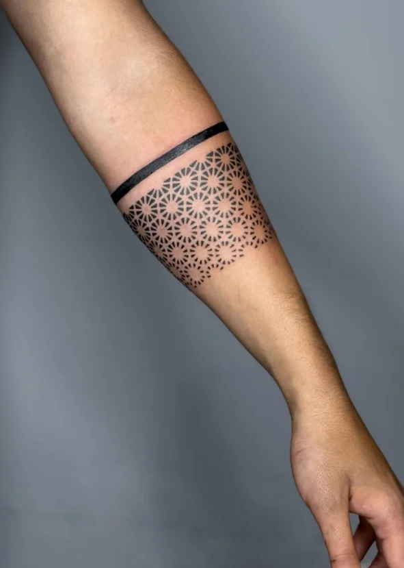 Geometric forearm tattoo featuring repeating lines and symmetrical shapes wrapping around the arm