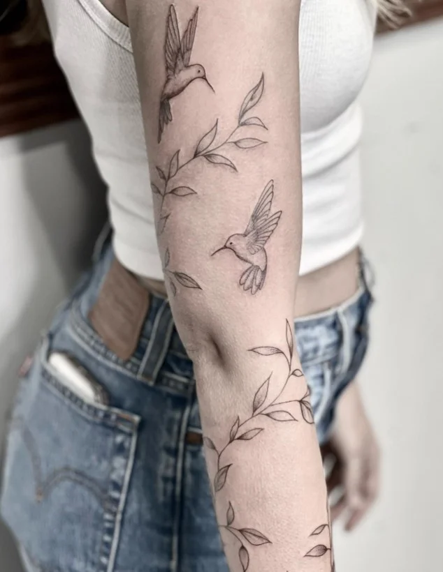 Hummingbird and flower wrap around arm tattoo with delicate botanical details
