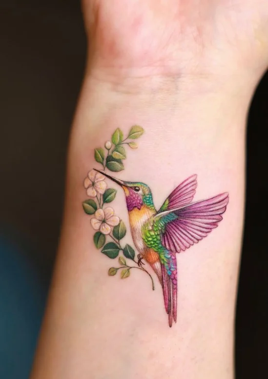 Hummingbird forearm tattoo with detailed wings and small floral elements