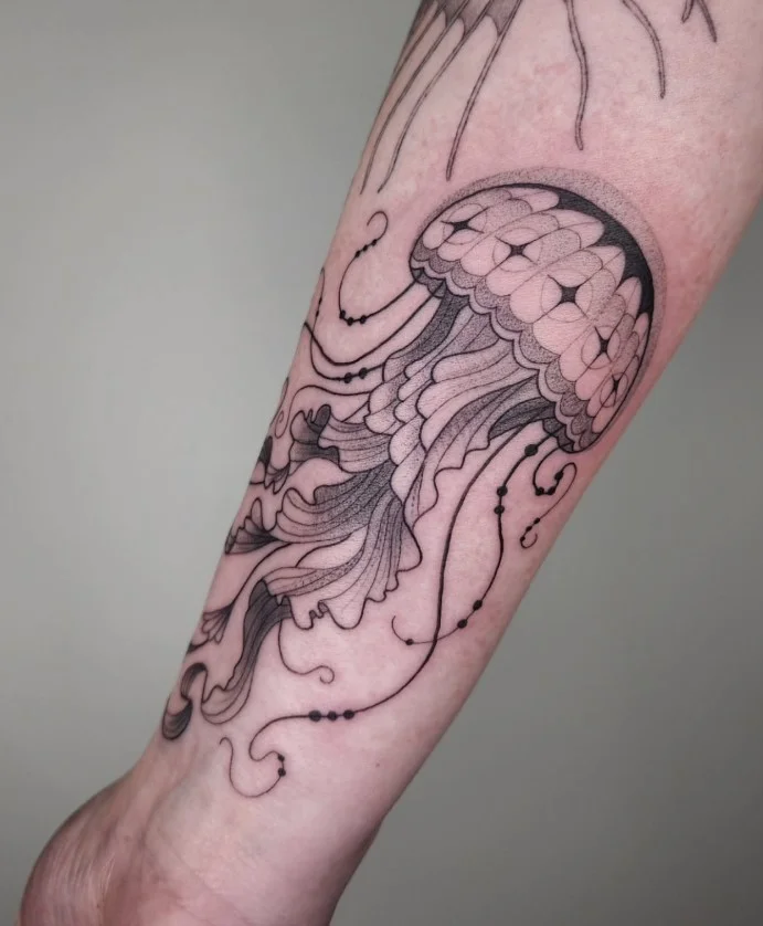 Detailed jellyfish tattoo with flowing tentacles curving around a woman's forearm