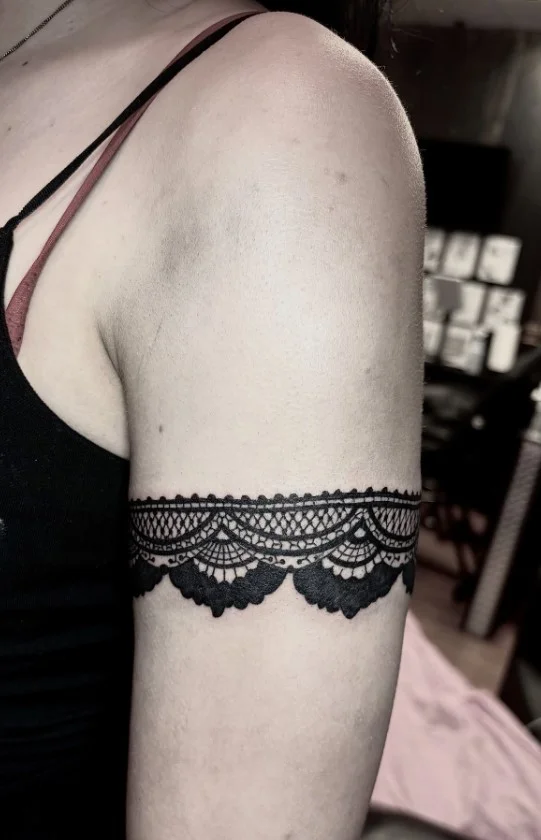 Lace-inspired wrap around bicep tattoo with delicate ornamental patterns and open space