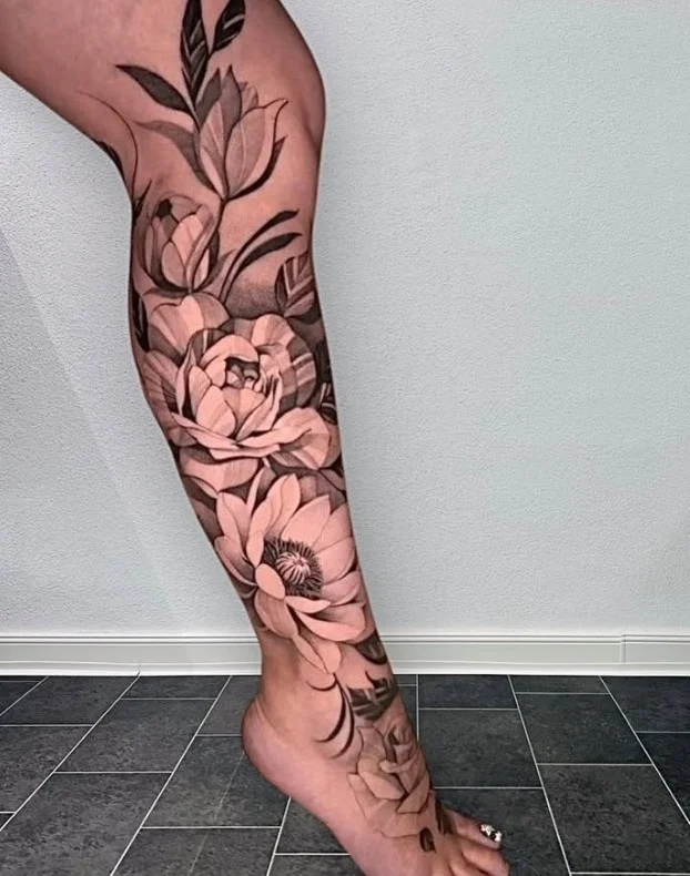 Large floral lower leg tattoo with a bold central flower and foliage