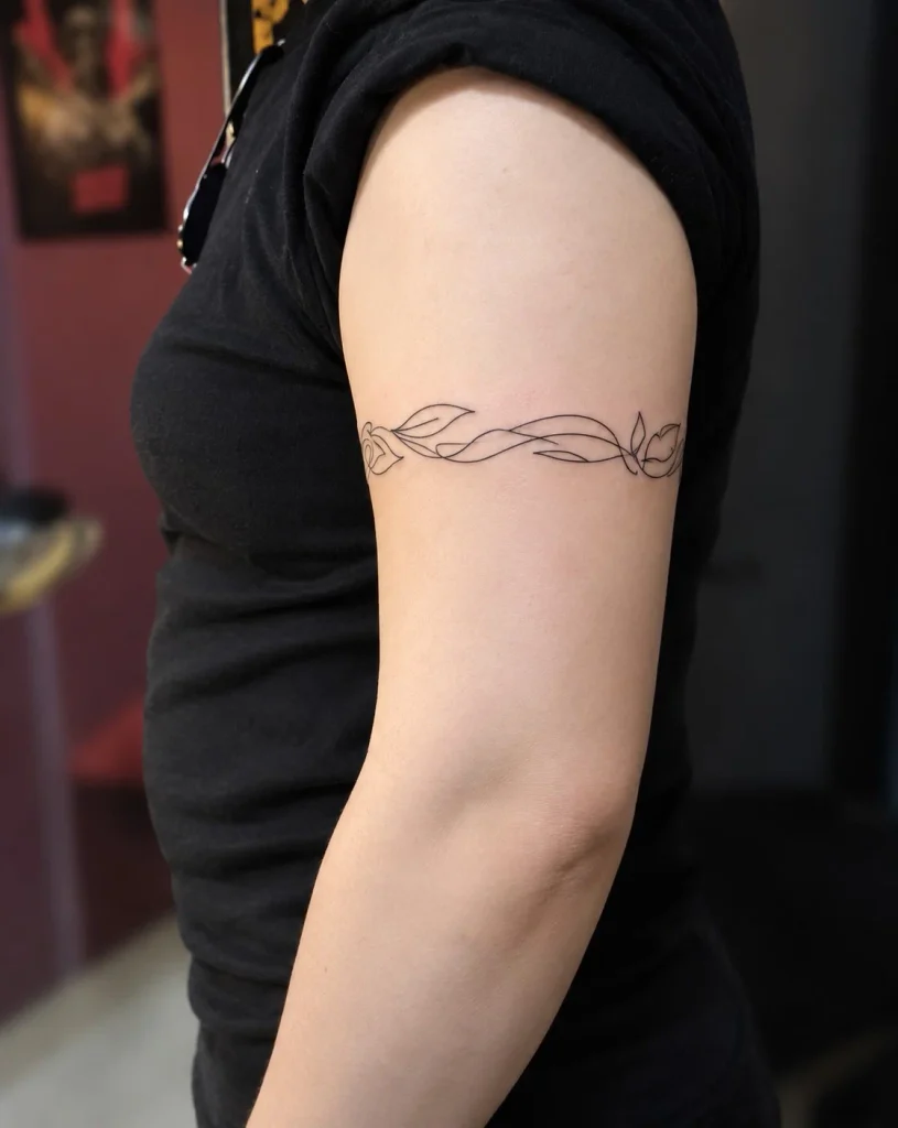 Minimalist continuous-line bicep wrap tattoo with delicate curves and small symbols