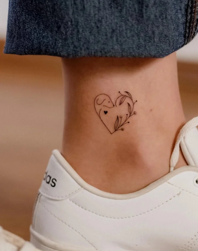 Minimalist fine line heart ankle tattoo featuring a small simple heart outline positioned delicately above the ankle