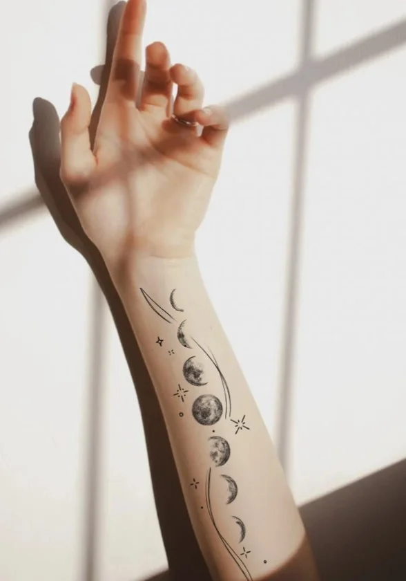Crescent moon with small stars forming a delicate celestial tattoo around a woman's forearm